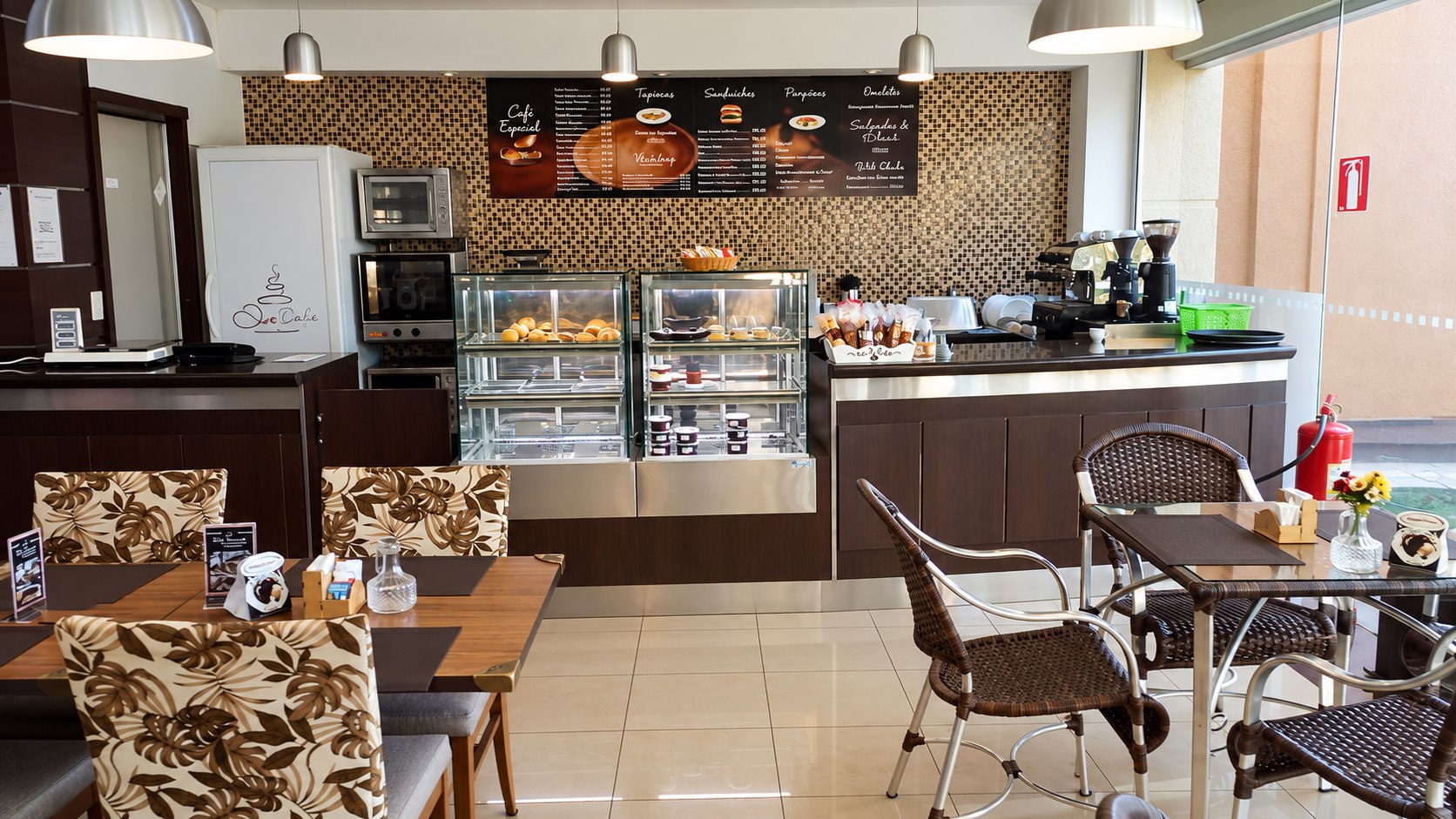 Salão da cafeteria com balcão de vitrines, mesas e área de atendimento