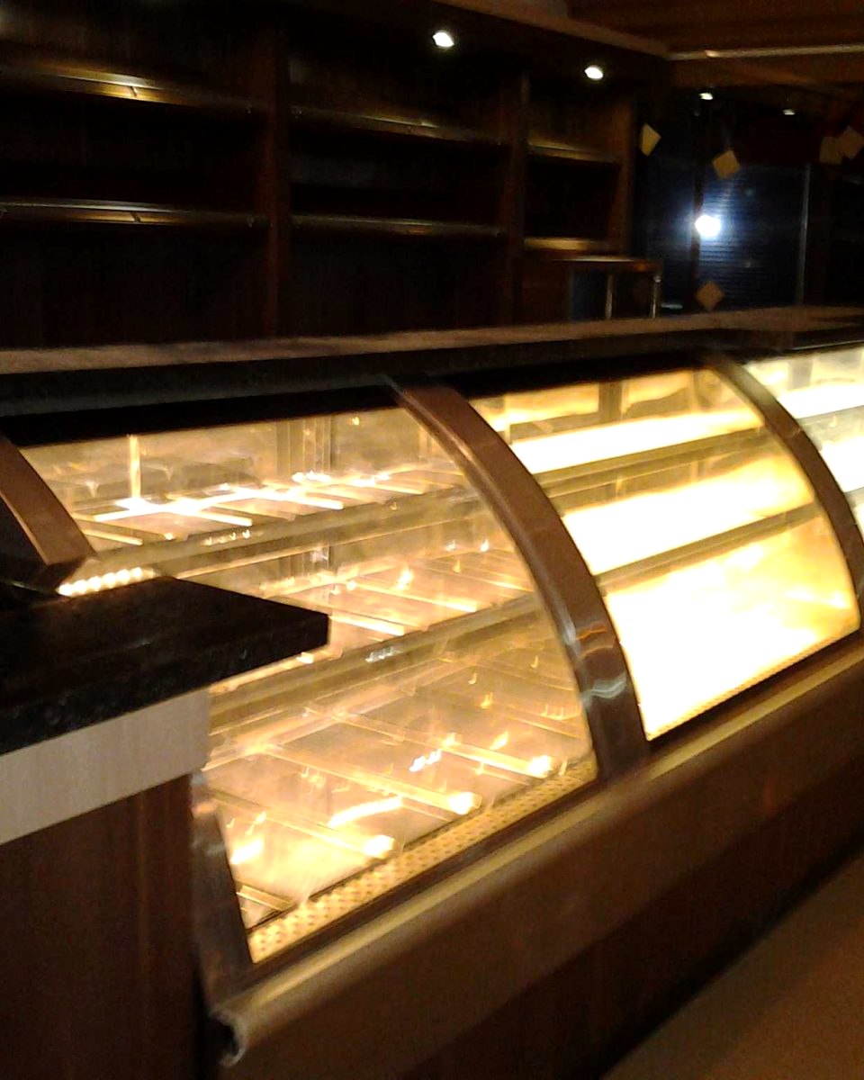 Vitrine de vidro curvo iluminada, com doces em exposição