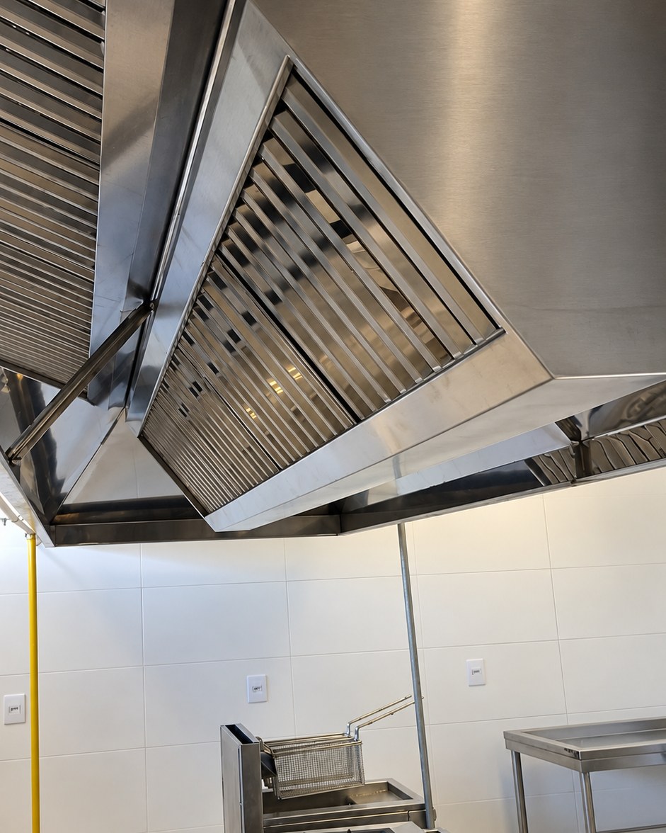 Coifa industrial em aço inox vista por baixo, com filtros e a linha de cocção embaixo