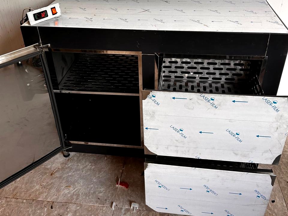 Balcão refrigerado com porta e gavetas abertas, mostrando as prateleiras internas em aço inox