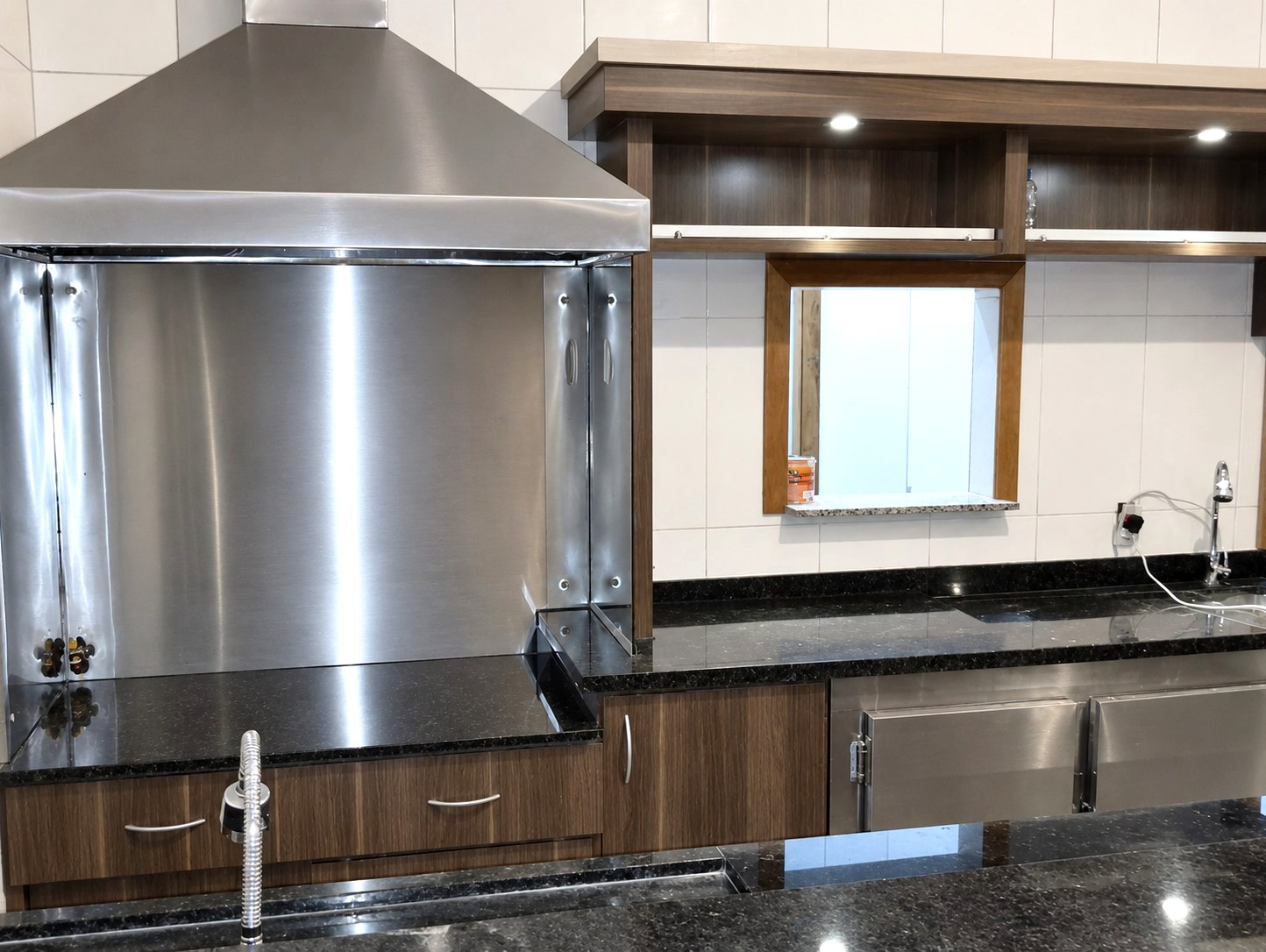 Área gourmet com churrasqueira em aço inox embutida na marcenaria, tampo de granito e cuba