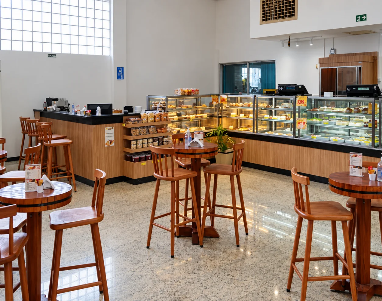 Área de mesas com banquetas de madeira, balcão de café e vitrines refrigeradas